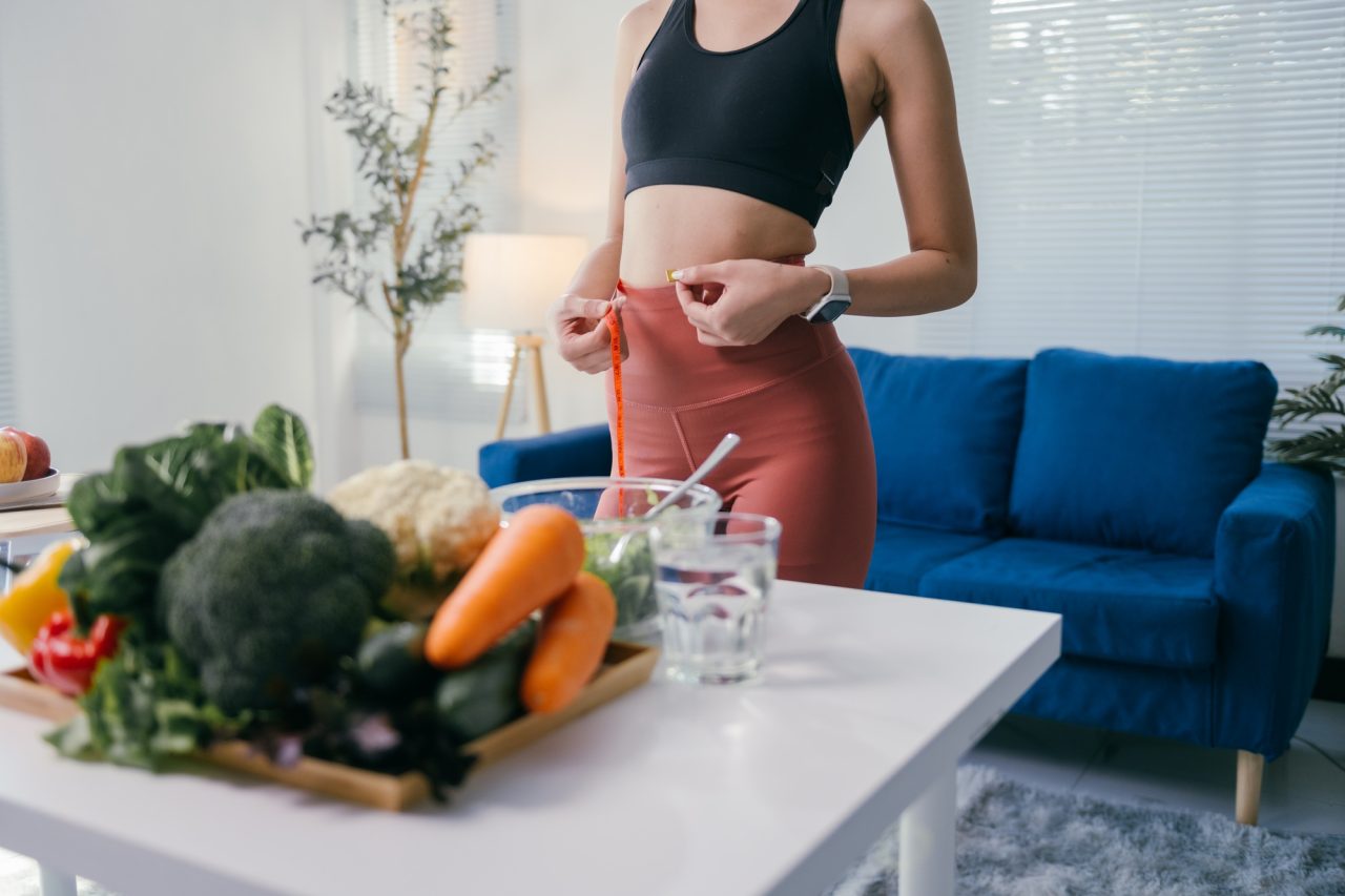 young woman measuring her waistline with tape measure after having a healthy meal with vegetables an